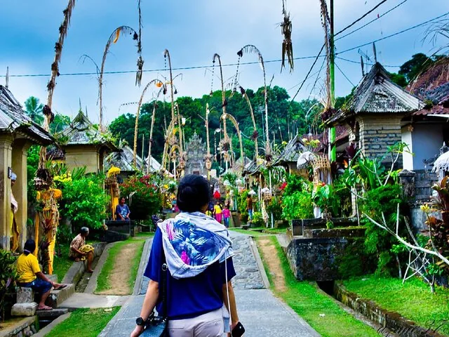 A person walking down a path in a Balinese village decorated for a festival.