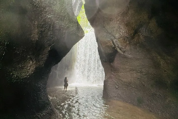Eine Person, die in der Nähe eines Wasserfalls steht, der durch eine Felsspalte sichtbar ist.