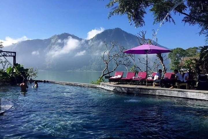 Persone che si rilassano in una piscina a sfioro con vista su un lago e una montagna.
