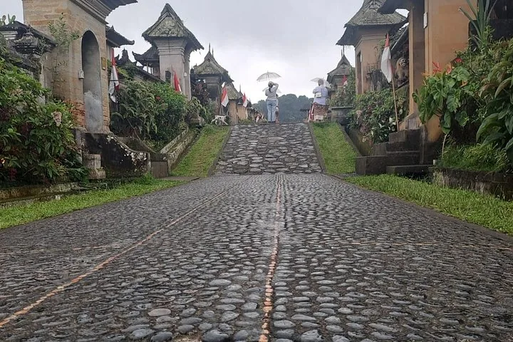 Eine nasse Kopfsteinpflasterstraße, die in einem traditionellen balinesischen Dorf bergauf führt.